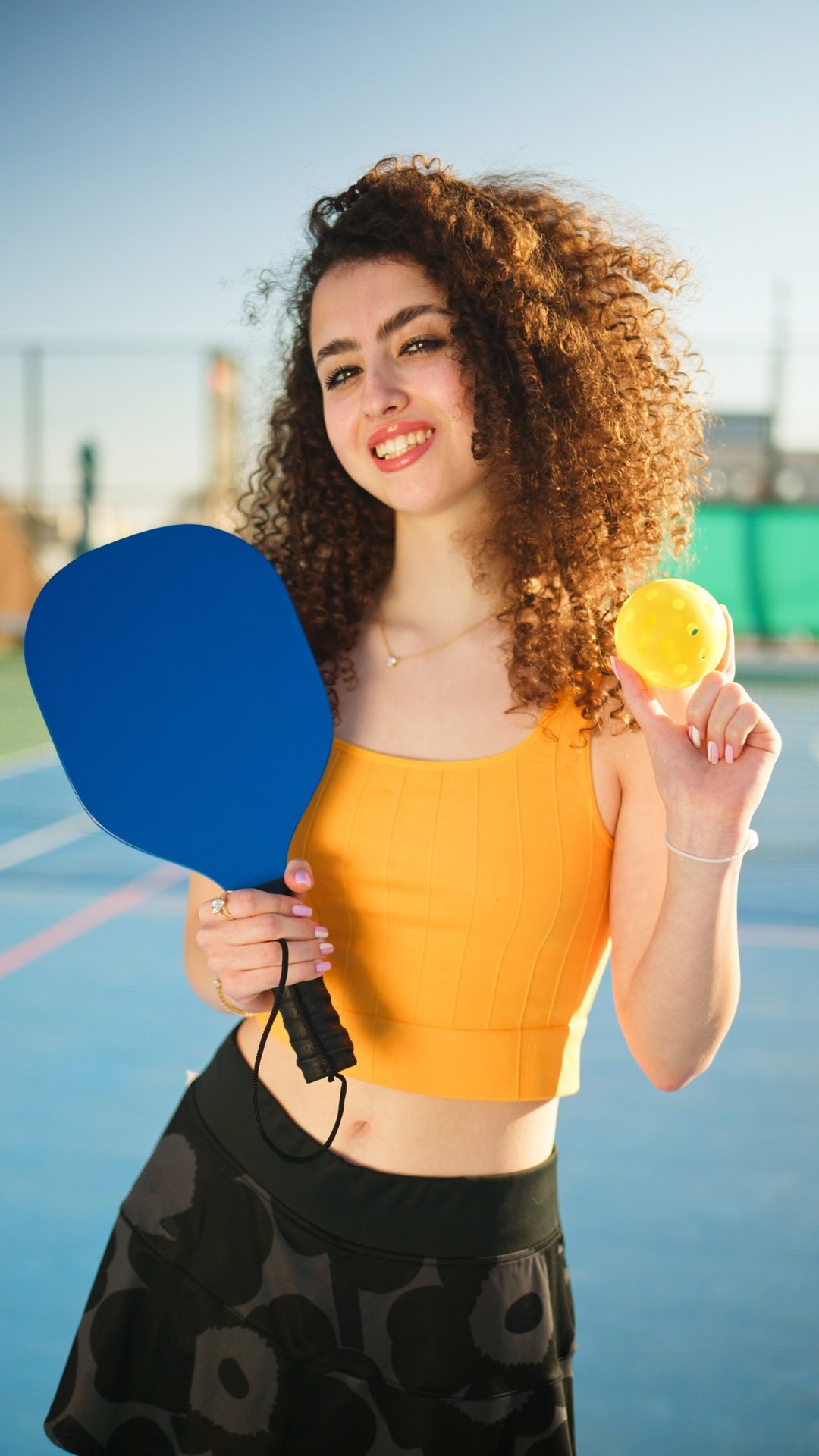 Portait of a young, happy and smiling curly haired girl holding pickleball paddle